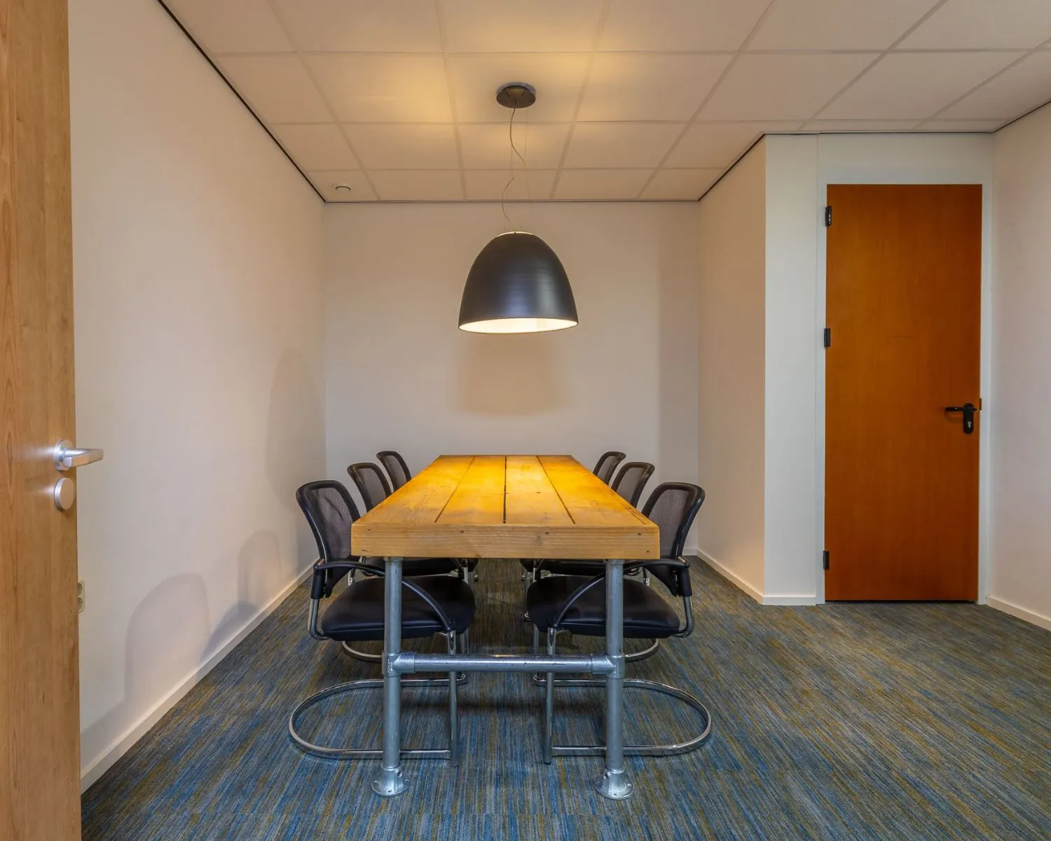 Vergaderruimte met houten tafel, zes stoelen en industriële hanglamp in kantoor aan de Mozartlaan 27 in Hilversum.
