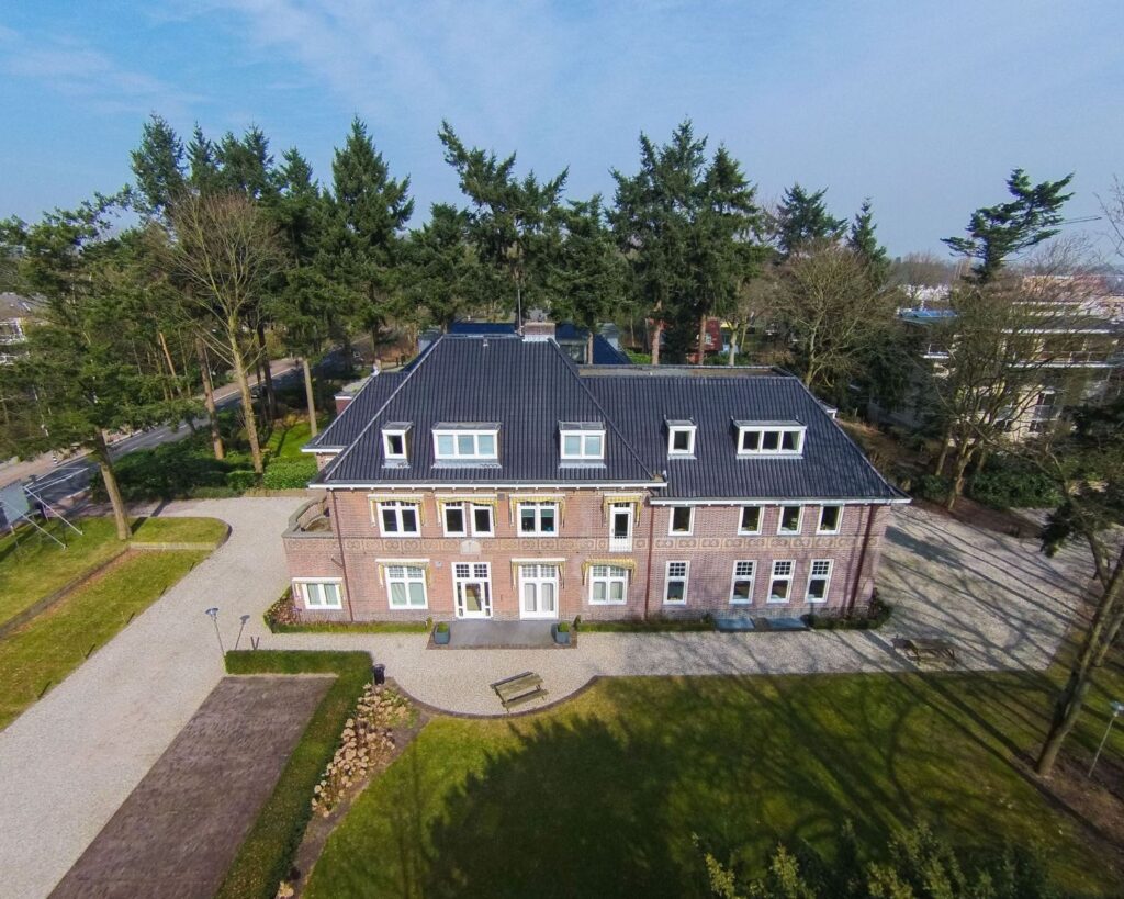 Luchtfoto van een karakteristiek kantoorpand aan de Utrechtseweg 47 in Hilversum, omringd door bomen en een ruime oprijlaan.