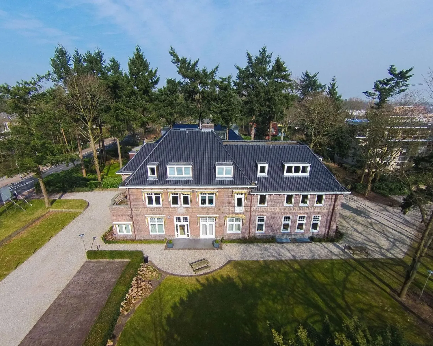 Luchtfoto van een karakteristiek kantoorpand aan de Utrechtseweg 47 in Hilversum, omringd door bomen en een ruime oprijlaan.