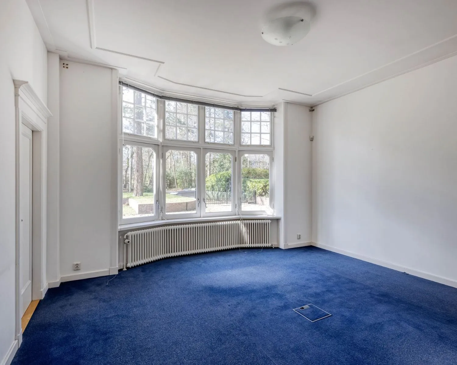 Lichte kantoorruimte met blauw tapijt en grote raampartij aan de Utrechtseweg 47 in Hilversum.