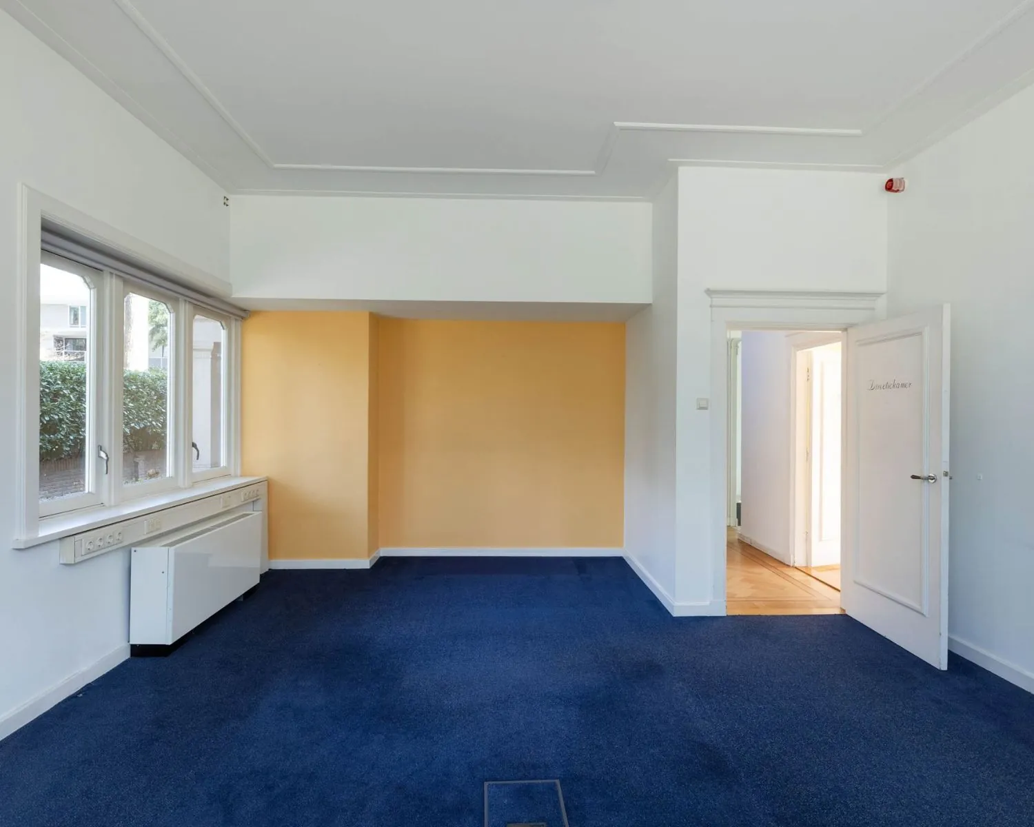 Leegstaand kantoor met blauw tapijt, geelgekleurde muur en open deur aan de Utrechtseweg 47 in Hilversum.