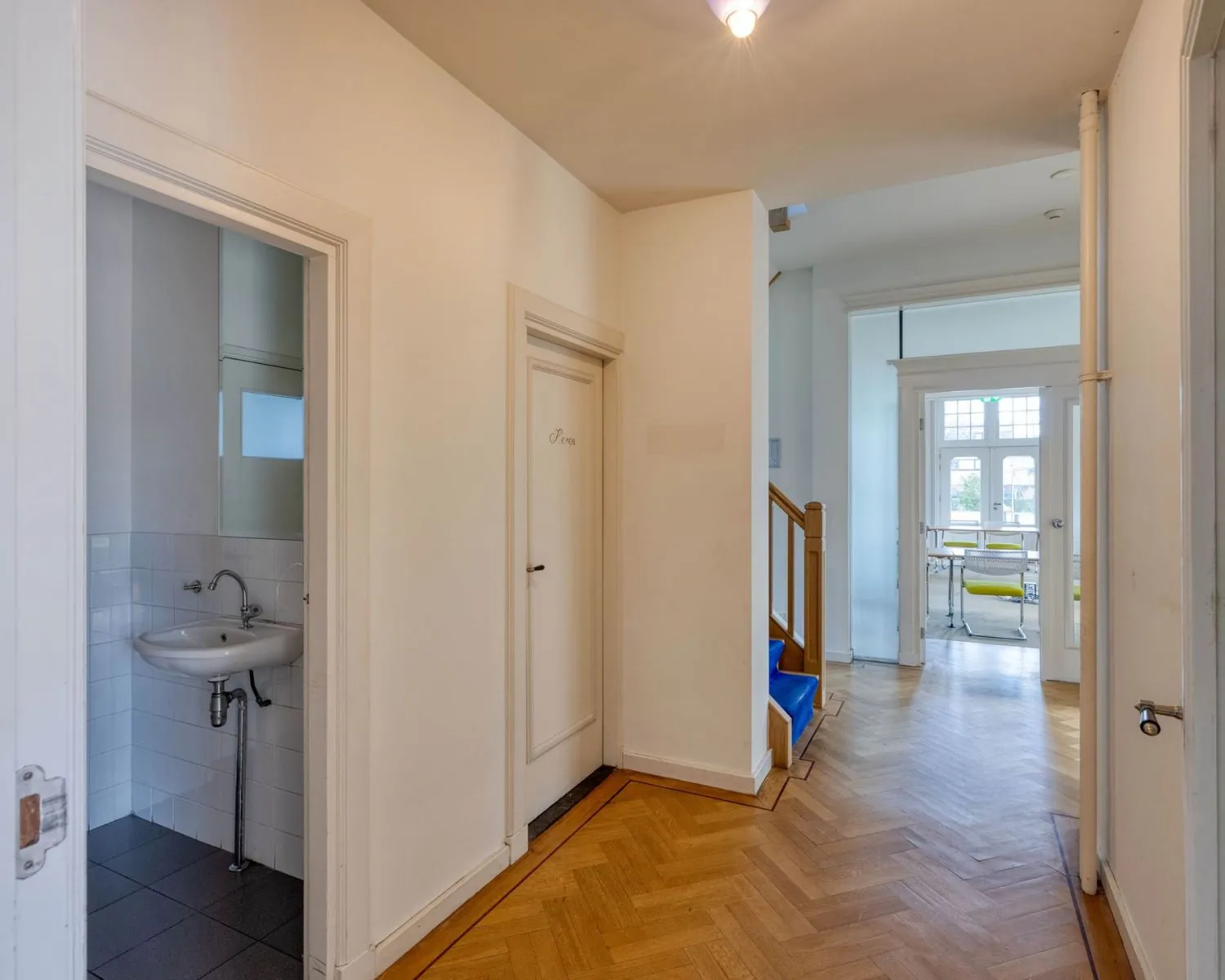 Hal met houten visgraatvloer, zicht op trap, toilet en kantoorruimte aan de Utrechtseweg 47 in Hilversum.