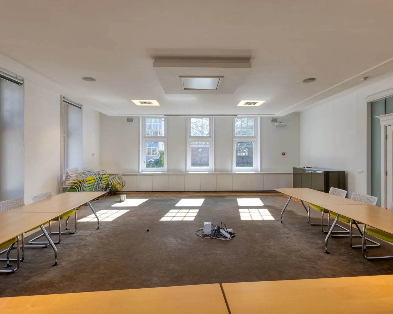 Vergaderruimte met grote ramen, U-vormige opstelling van tafels en stapel stoelen aan de zijkant in een kantoorpand aan de Utrechtseweg 47 in Hilversum.
