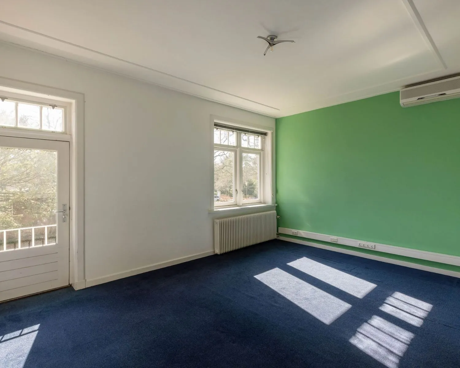Lichte kantoorruimte met groene accentmuur en blauwe vloerbedekking aan de Utrechtseweg 47 in Hilversum.