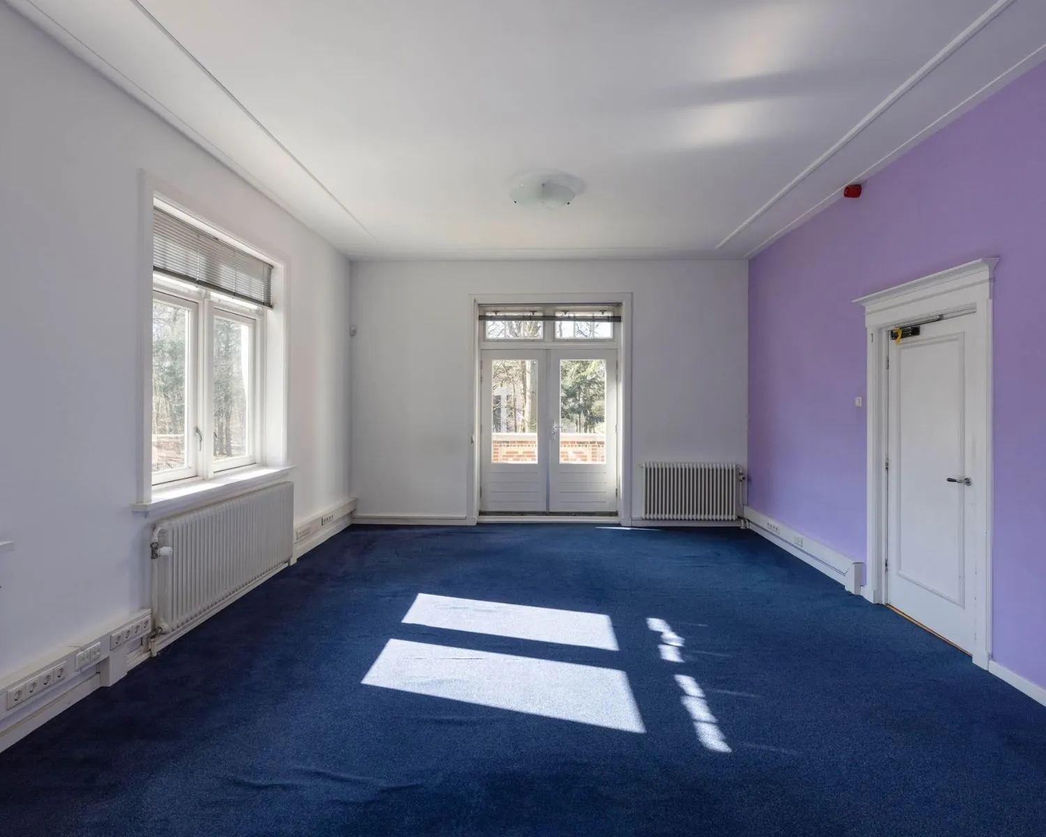 Lichte kantoorruimte met paarse accentmuur en blauwe vloerbedekking aan de Utrechtseweg 47 in Hilversum.