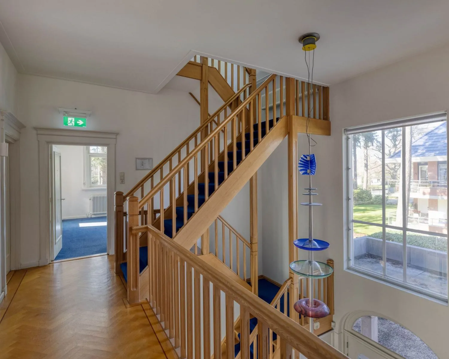 Trappenhuis met houten leuning en blauwe vloerbedekking in een kantoorruimte aan de Utrechtseweg 47 in Hilversum.