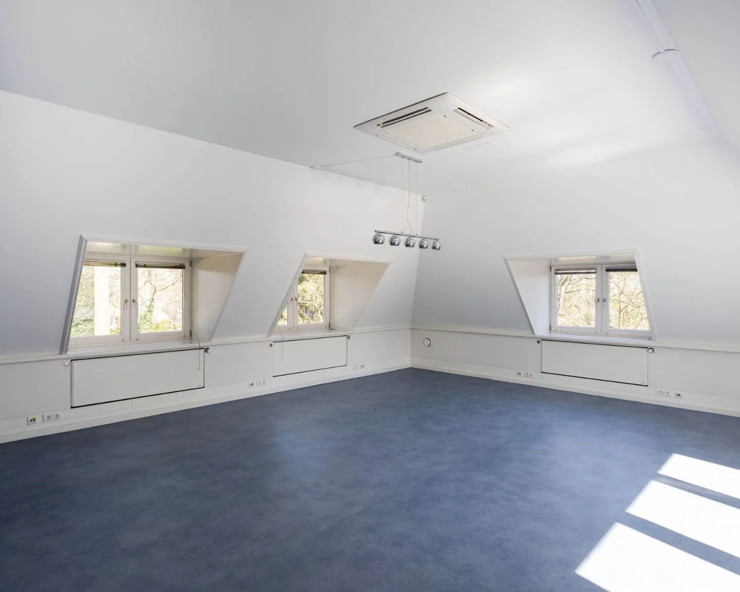 Lichte en ruime kantoorruimte met blauwe vloer en meerdere ramen aan de Utrechtseweg 47 in Hilversum.