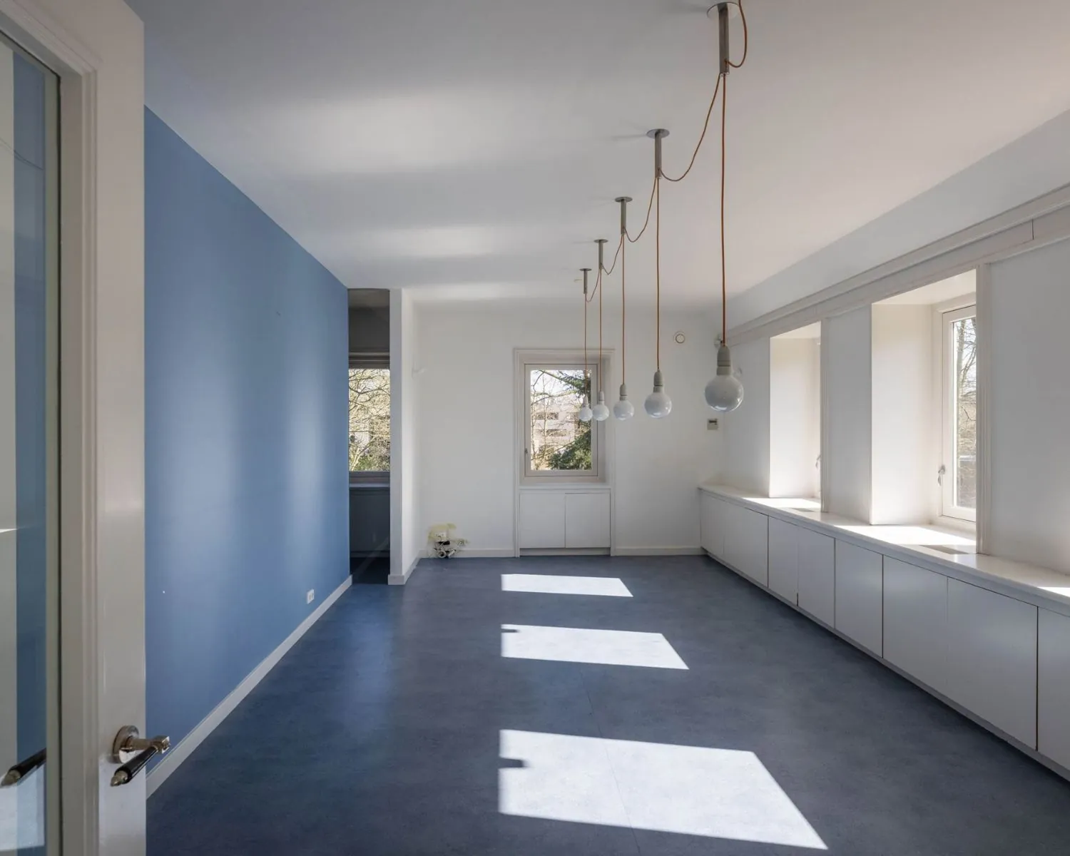 Lichte en moderne kantoorruimte aan de Utrechtseweg 47 in Hilversum met grote ramen, blauwe vloer en hanglampen.