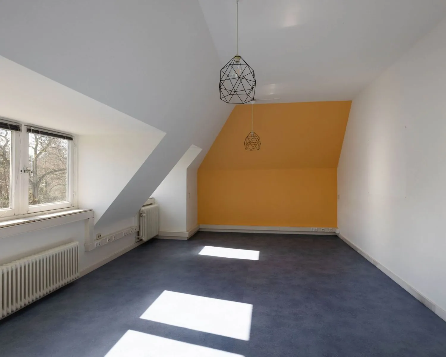 Lichte kantoorruimte met schuine wanden, een opvallende oranje accentmuur en grote ramen aan de Utrechtseweg 47 in Hilversum.