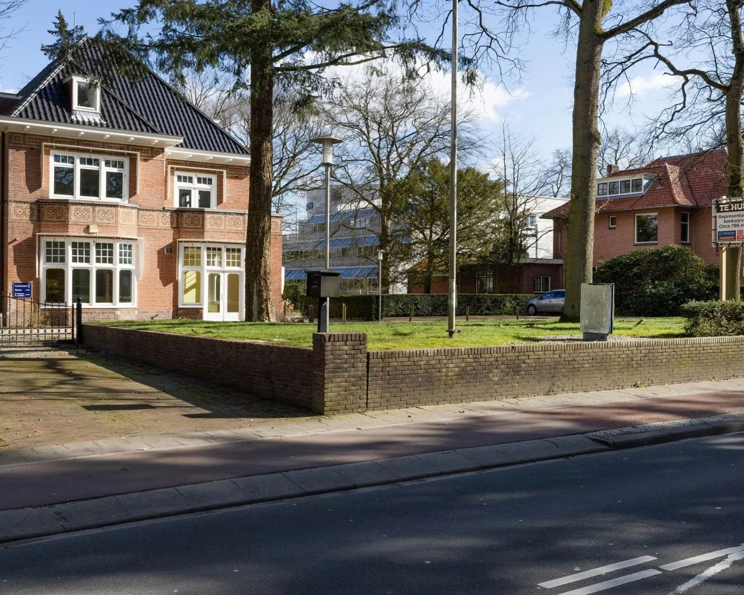 Vooraanzicht van een karakteristiek kantoorpand aan de Utrechtseweg 47 in Hilversum met tuin en 'te huur'-bord.