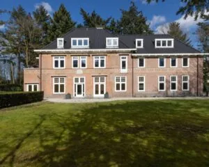 Vooraanzicht van een statig kantoorgebouw aan de Utrechtseweg 47 in Hilversum, omgeven door groen en bos.