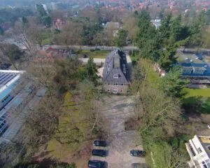 Luchtfoto van een kantoorpand aan de Utrechtseweg 47 in Hilversum, omringd door bomen en parkeerplaatsen.