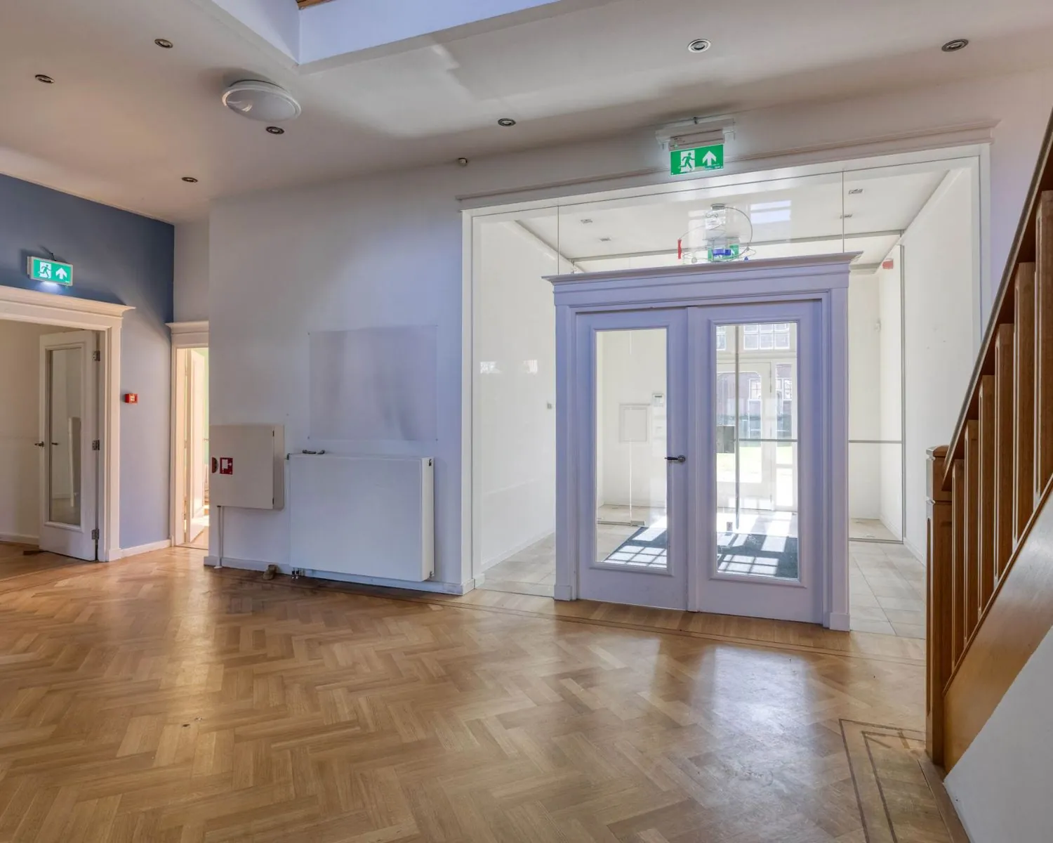 Hal met houten vloer, trap en glazen deuren in kantoorruimte aan de Utrechtseweg 47 in Hilversum.