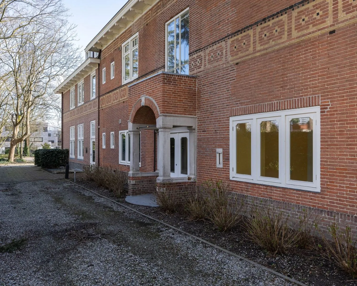 Vooraanzicht van een karakteristiek kantoorpand aan de Utrechtseweg 47 in Hilversum met rode bakstenen, witte kozijnen en een gemetselde boogentree.