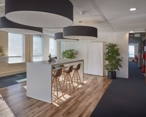 Moderne kantoorruimte aan de Hogehilweg 24 met hoge plafonds, een lange vergadertafel, grote lampen en veel natuurlijk licht.