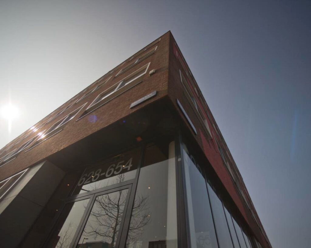 Hoekpand met glazen entree aan de IJburglaan, huisnummers 628-654, gefotografeerd van onderaf in tegenlicht.