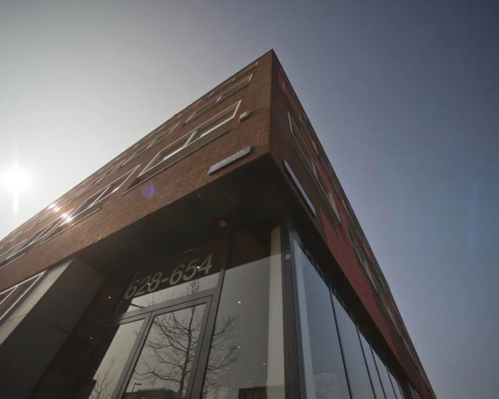 Hoekpand met glazen entree aan de IJburglaan, huisnummers 628-654, gefotografeerd van onderaf in tegenlicht.