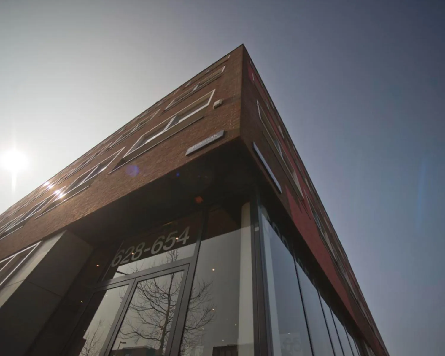 Hoekpand met glazen entree aan de IJburglaan, huisnummers 628-654, gefotografeerd van onderaf in tegenlicht.