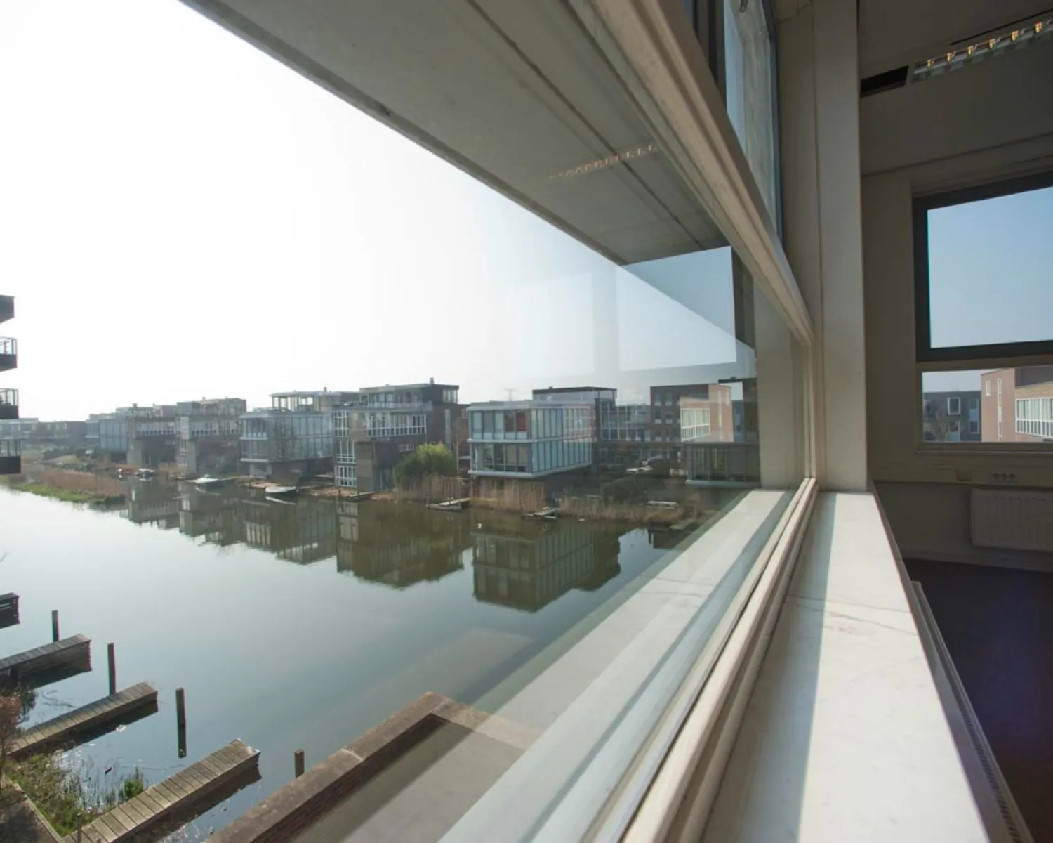 Uitzicht vanuit een kantoorruimte aan de IJburglaan op moderne waterwoningen en een rustige gracht.