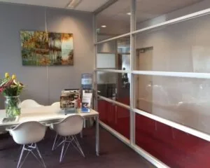 Moderne kantoorruimte aan de IJburglaan met glazen scheidingswand, witte stoelen, leestafel en watercooler.