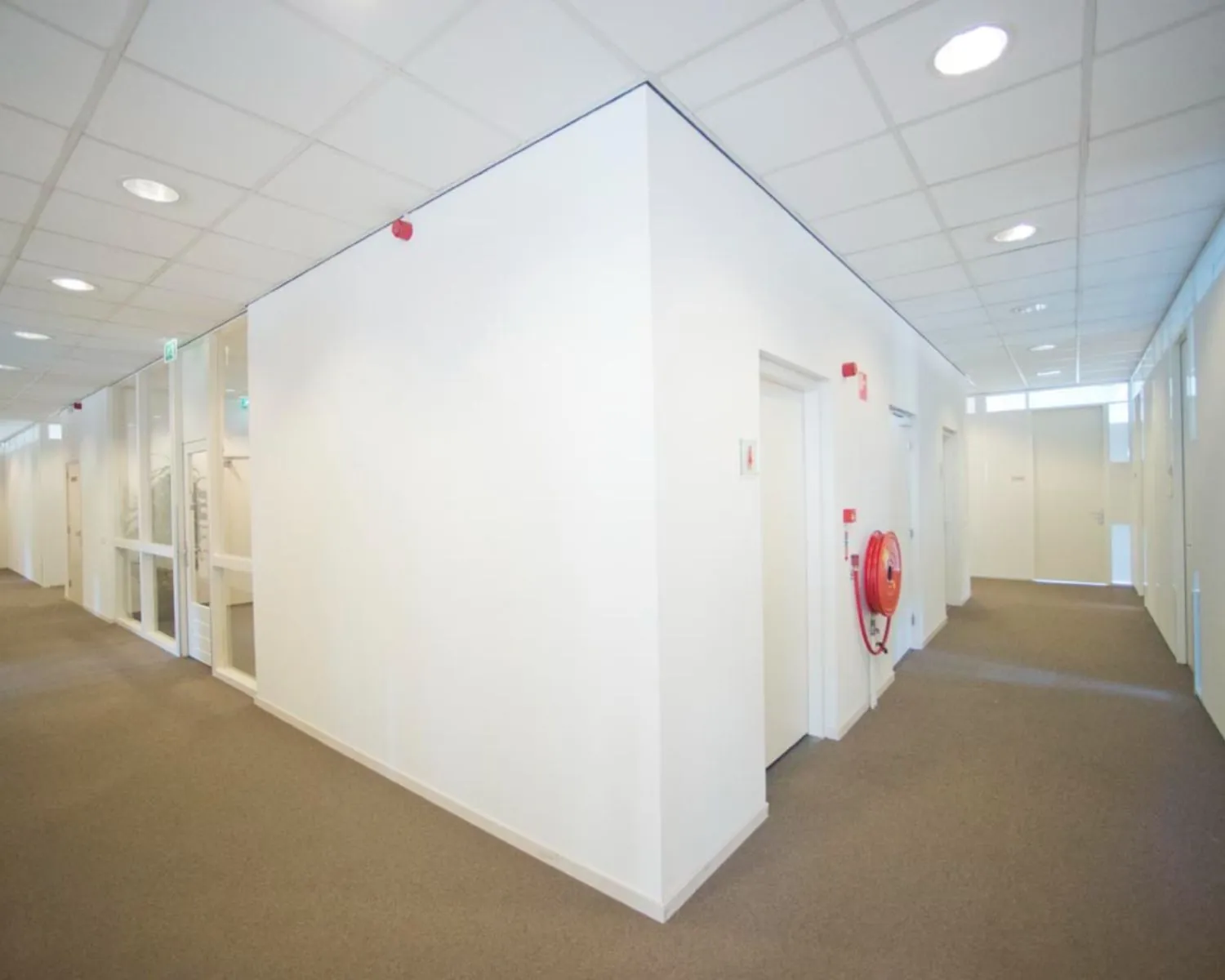 Verlichte gang met witte muren en deuren in een kantoorruimte aan de IJburglaan, met brandslanghaspel aan de muur.