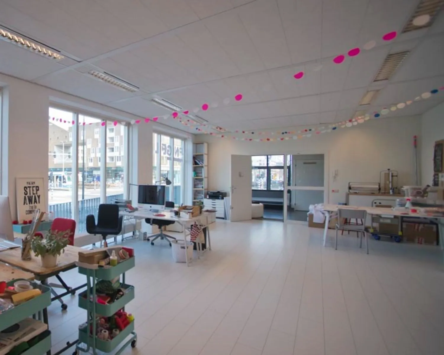 Lichte en ruime kantoorruimte aan de IJburglaan met werkplekken, grote ramen en kleurrijke slingers aan het plafond.