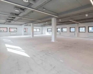 Lichte, open kantoorruimte te huur aan de Joop Geesinkweg met grote ramen en een industrieel plafond.
