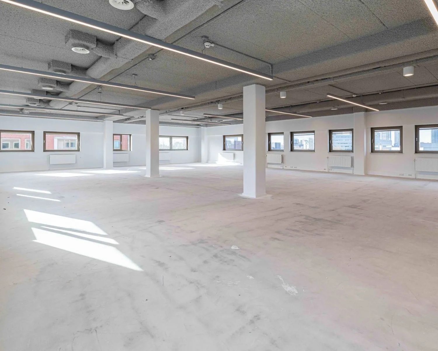 Lichte, open kantoorruimte te huur aan de Joop Geesinkweg met grote ramen en een industrieel plafond.