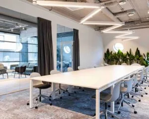 Moderne kantoorruimte aan de Joop Geesinkweg met lange vergadertafel, designstoelen, plantenwand en glazen vergaderruimtes.