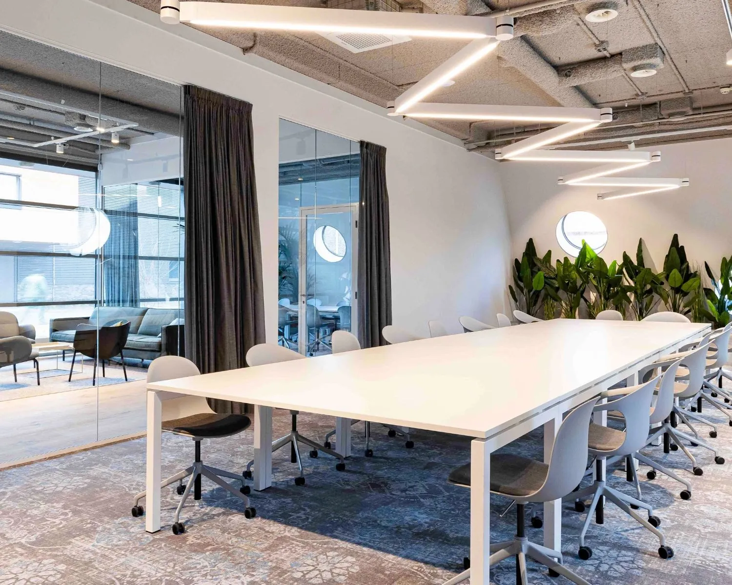 Moderne kantoorruimte aan de Joop Geesinkweg met lange vergadertafel, designstoelen, plantenwand en glazen vergaderruimtes.
