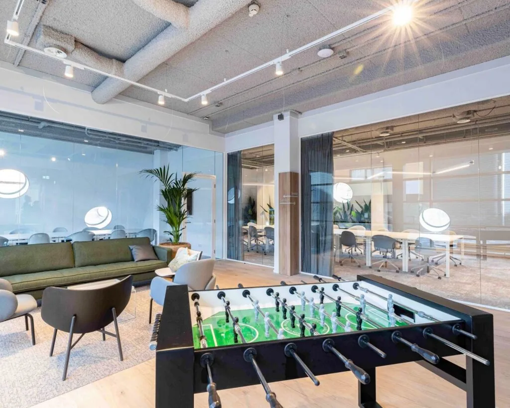 Moderne kantoorruimte aan de Joop Geesinkweg met glazen vergaderruimtes, loungehoek en een tafelvoetbaltafel.