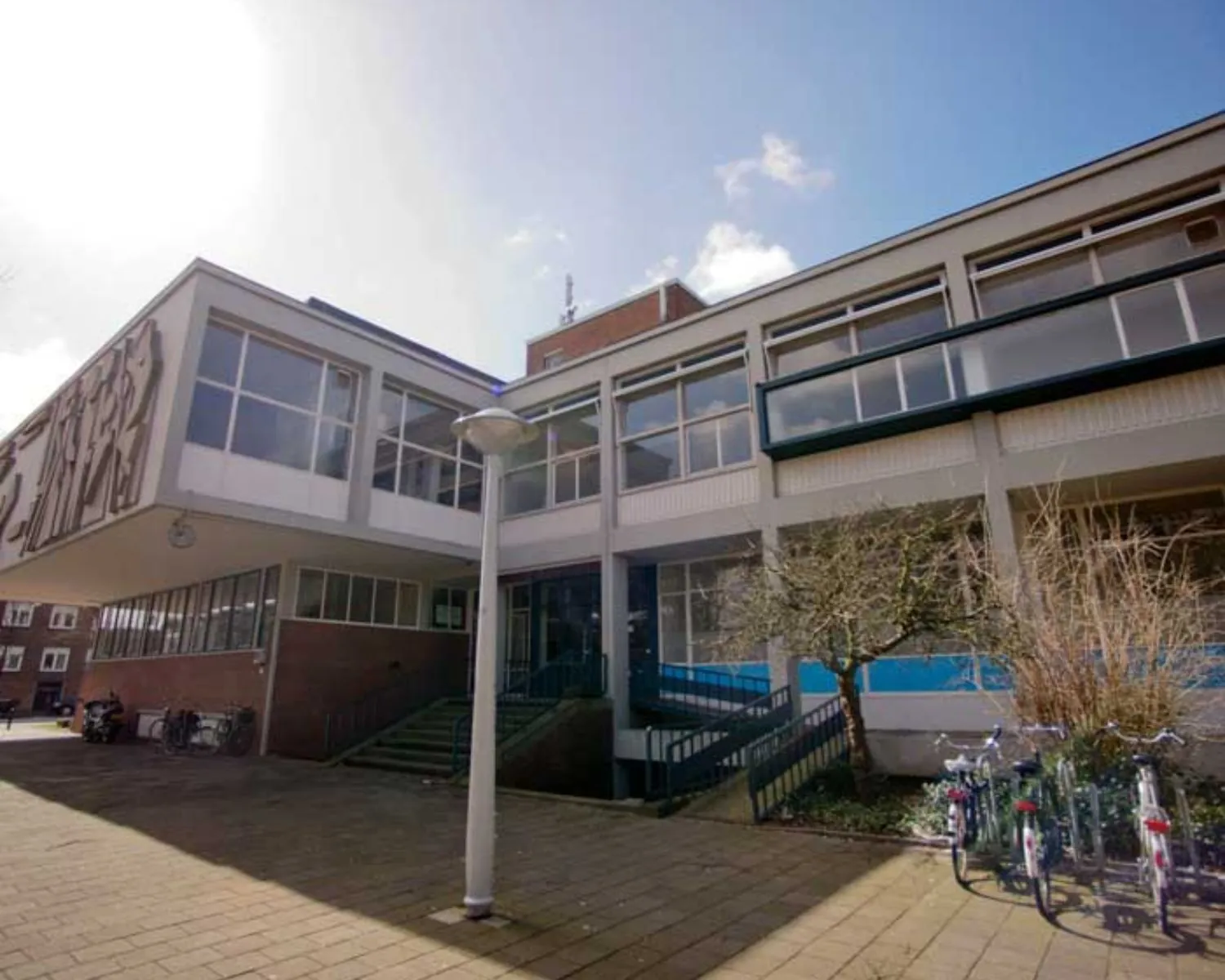 Vooraanzicht van een kantoorpand aan de Krelis Louwenstraat met brede ramen, een entree met trap en geparkeerde fietsen.