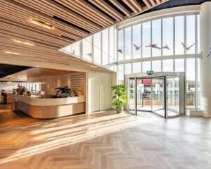 Moderne entreehal van kantoorgebouw Meander 901 in Arnhem met houten receptiebalie, draaiende glazen deur en veel natuurlijk licht.