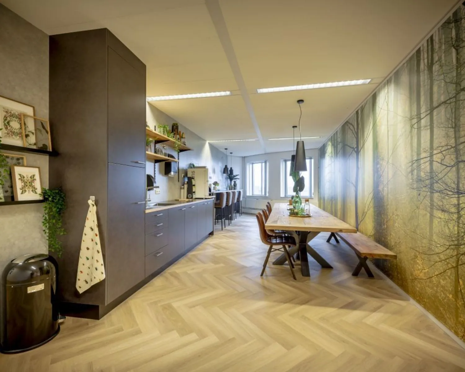 Moderne kantoorruimte in Arnhem met open keuken, lange houten vergadertafel en natuurwanddecoratie.