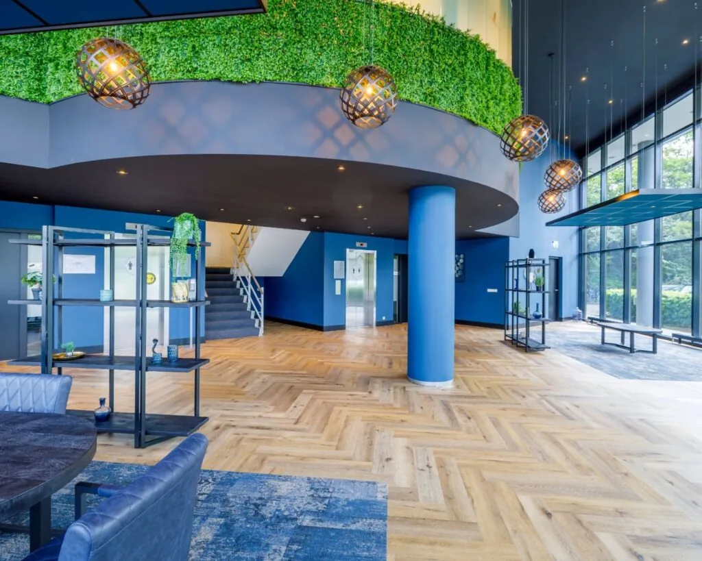 Moderne en lichte kantoorruimte aan de Overschiestraat 61 met houten visgraatvloer, grote raampartijen en groene wanddecoratie.