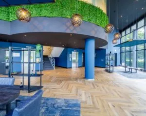 Moderne en lichte kantoorruimte aan de Overschiestraat 61 met houten visgraatvloer, grote raampartijen en groene wanddecoratie.