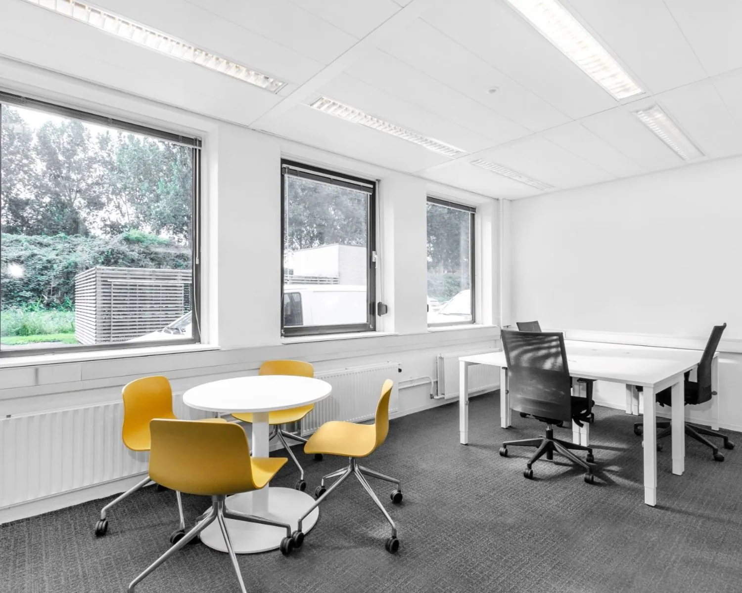 Moderne kantoorruimte aan de Paterswoldseweg met grote ramen, witte bureaus en gele vergaderstoelen.