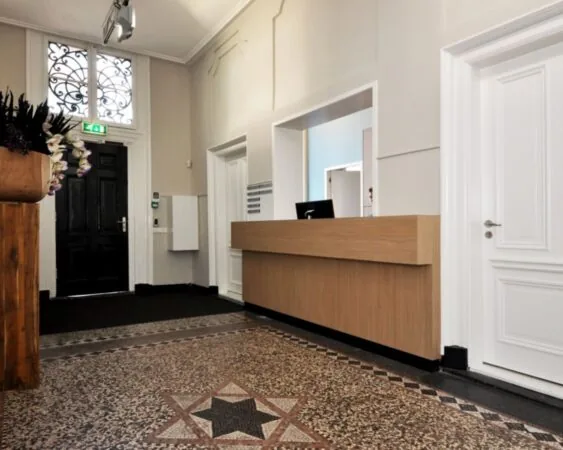 Moderne ontvangsthal met houten balie, mozaïekvloer en hoge plafonds in kantoorruimte aan Rapenburg 173.