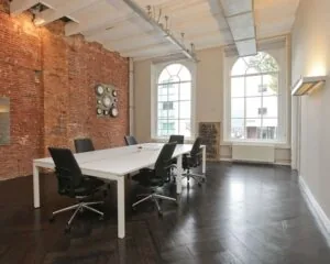 Moderne kantoorruimte aan de Rapenburgerstraat met hoge plafonds, bakstenen muur en grote ramen.