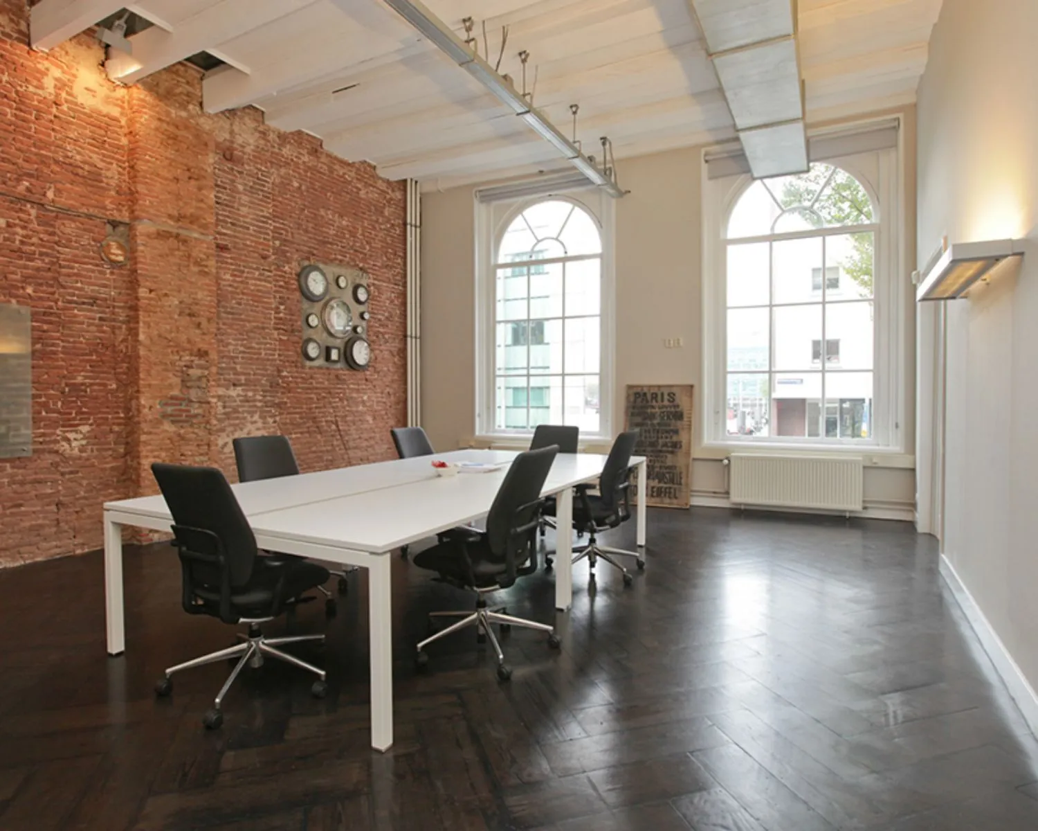Moderne kantoorruimte aan de Rapenburgerstraat met hoge plafonds, bakstenen muur en grote ramen.