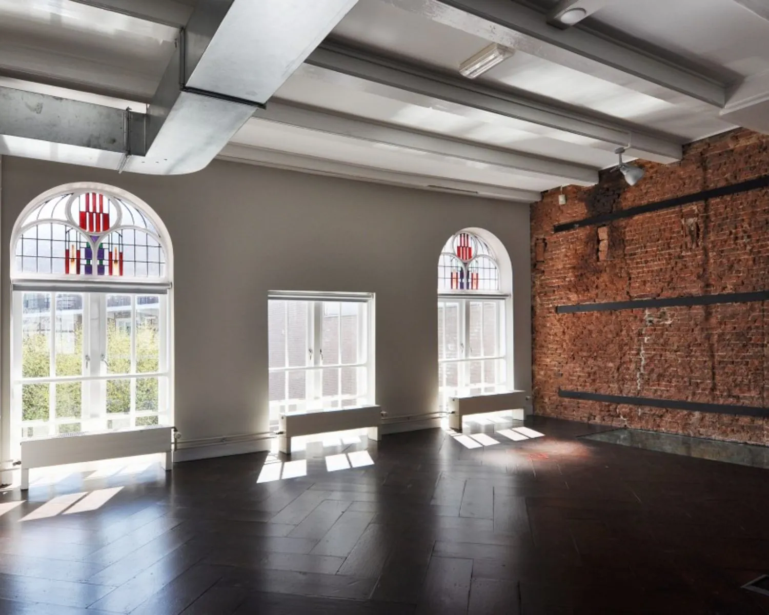 Lichte kantoorruimte te huur aan de Rapenburg met grote ramen, een bakstenen muur en industrieel plafond.