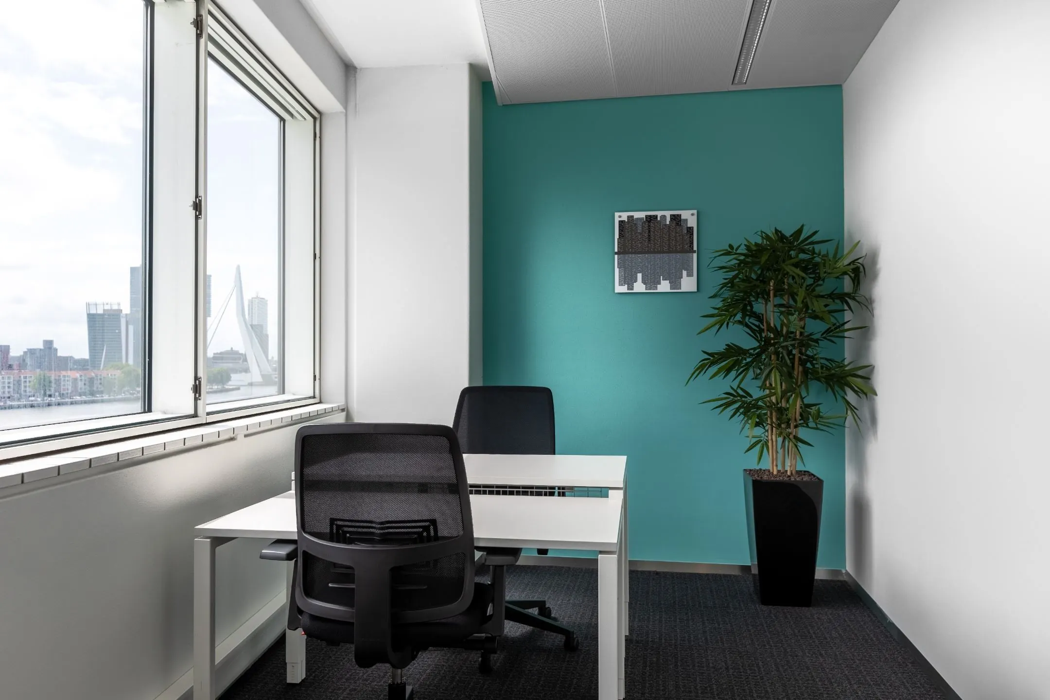 Moderne kantoorruimte met twee bureaus, uitzicht op de Erasmusbrug en een turquoise achterwand, gelegen aan Boompjes 40 in Rotterdam.