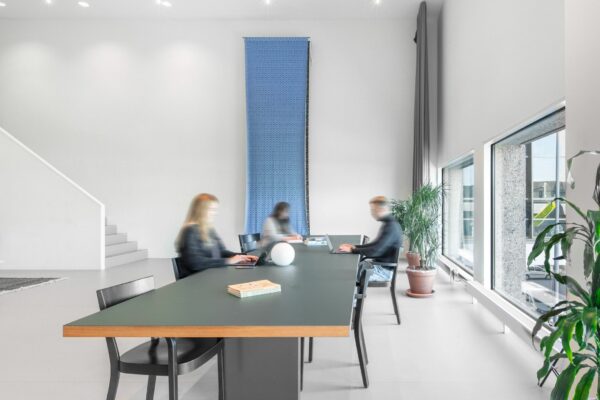 Moderne kantoorruimte in Rotterdam Hofplein 20 met grote ramen, minimalistische inrichting en werkende mensen aan een lange tafel.