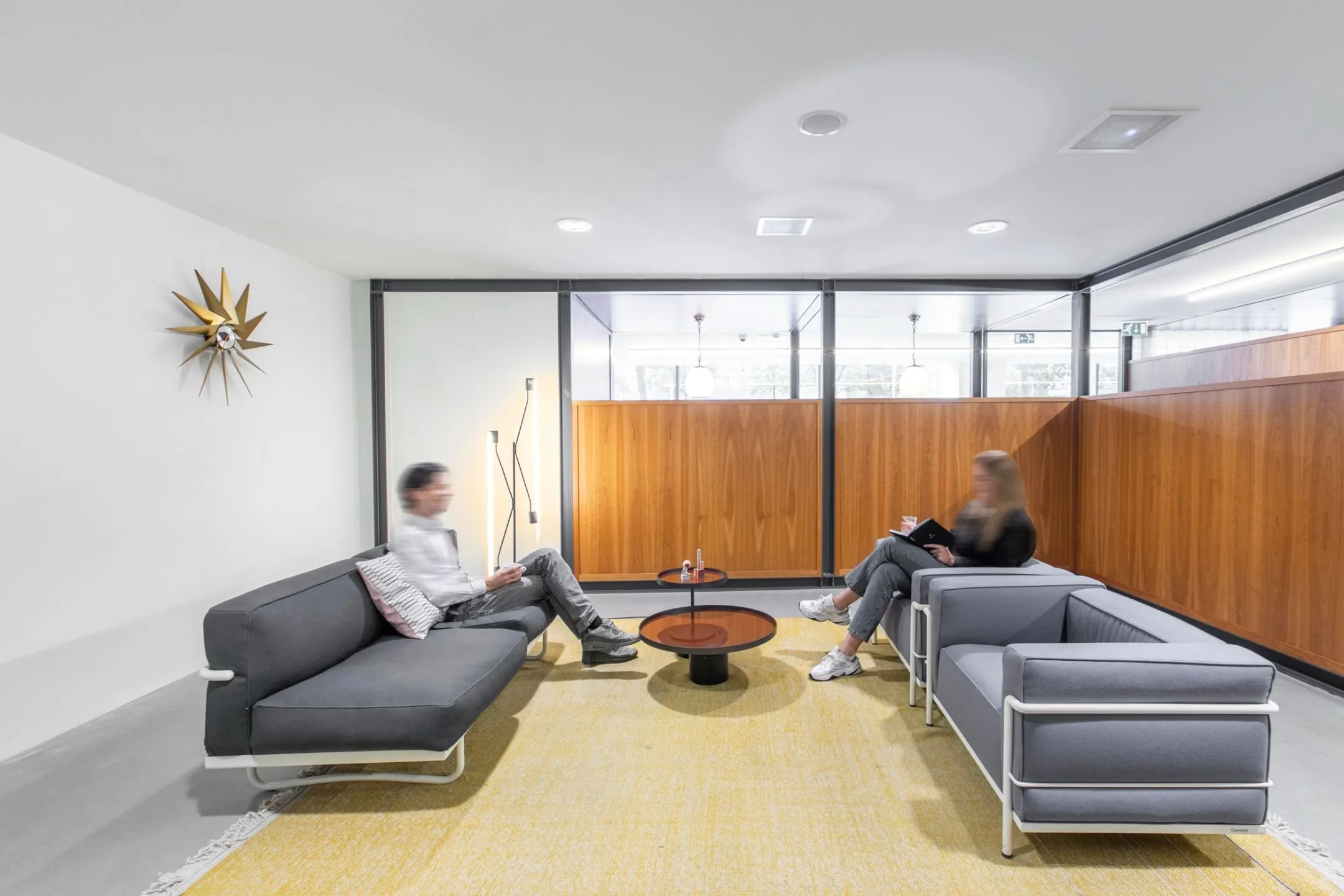 Moderne wachtruimte in kantoorruimte aan Hofplein 20 in Rotterdam met twee personen op grijze designbanken.