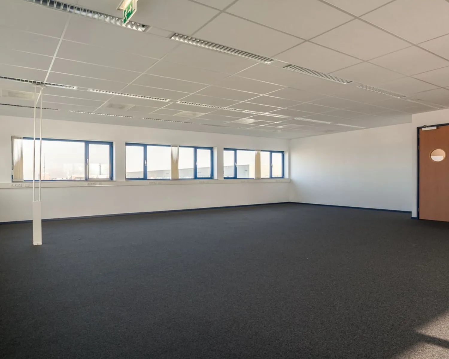 Lege kantoorruimte met systeemplafond en blauw omlijste ramen aan de Capronilaan in Schiphol-Rijk.