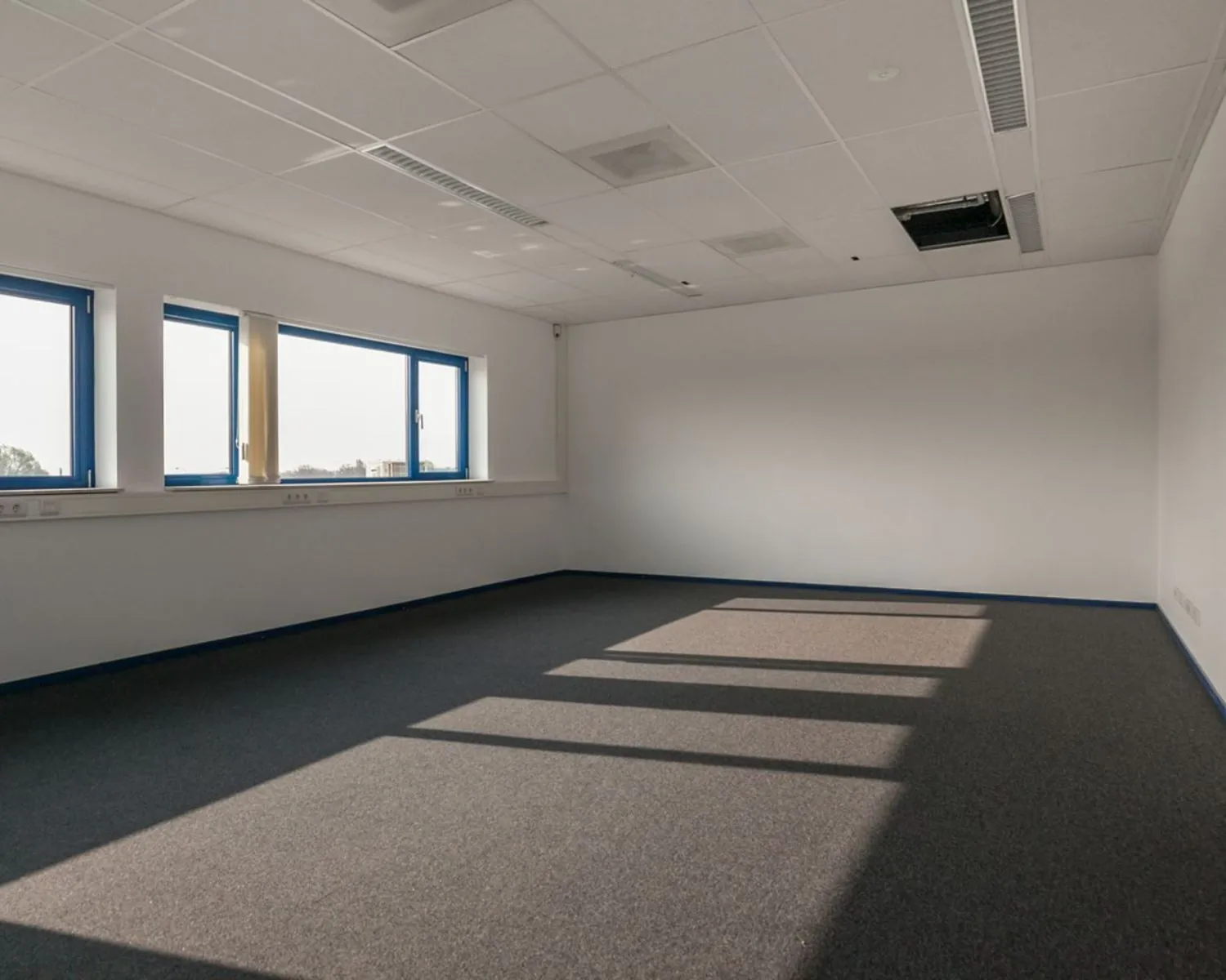 Leegstaand kantoor met grijze vloerbedekking en blauwomrande ramen aan de Capronilaan in Schiphol-Rijk.