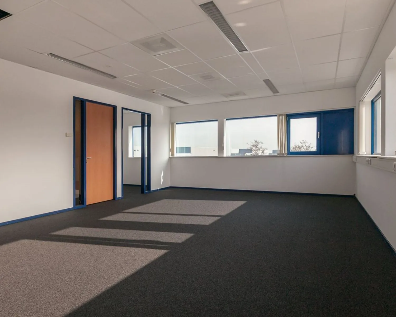 Lichte, lege kantoorruimte met ramen en blauwe kozijnen aan de Capronilaan in Schiphol-Rijk.