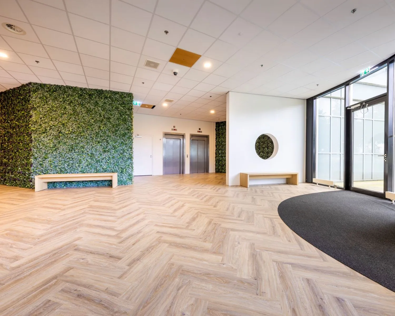Moderne entreehal van kantoorruimte aan de Tupolevlaan met houten visgraatvloer, groene wand en twee liften.