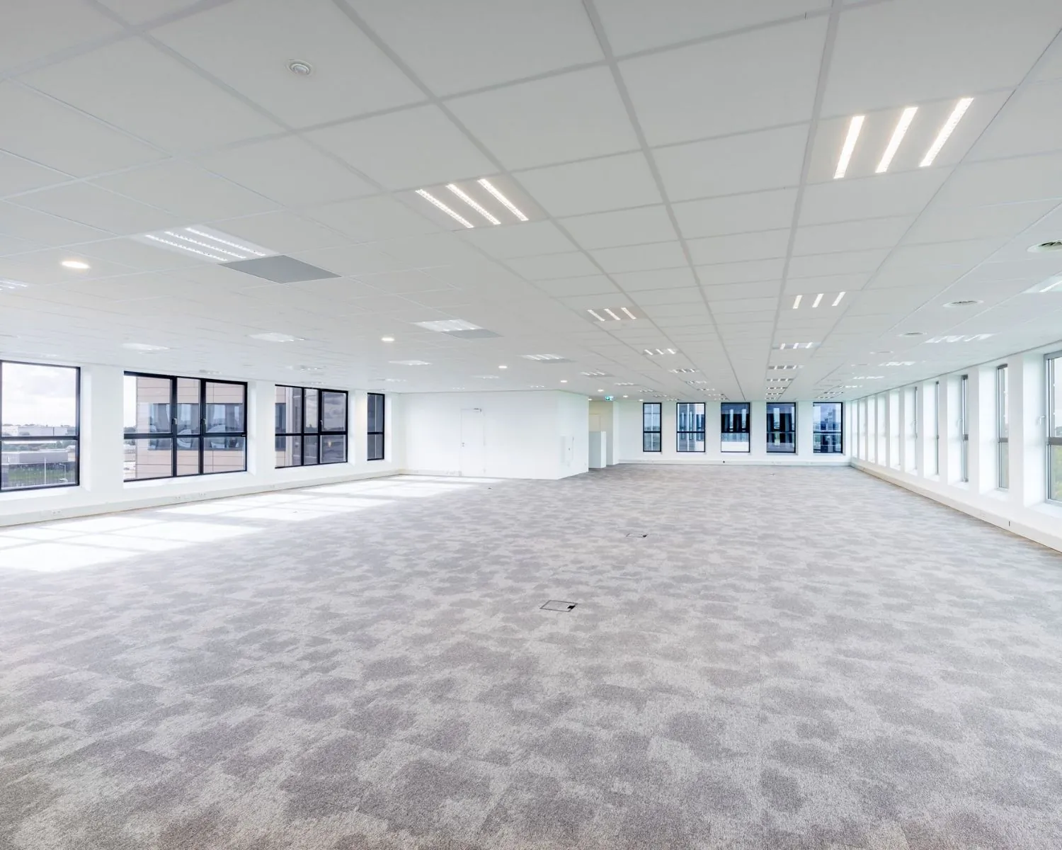 Ruime, lichte kantoorruimte met tapijtvloer en grote ramen aan de Tupolevlaan 2-24.