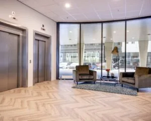 Moderne entree van een kantoorruimte aan de Tupolevlaan met zithoek, grote ramen en twee liften.